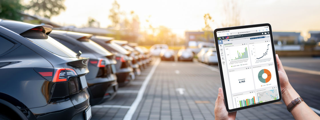 Fleet manager using a tablet with fleet management software, analyzing data while overseeing a parking lot filled with fleet vehicles.