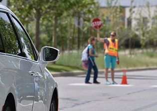 White car waiting for child to cross street with safety patrol